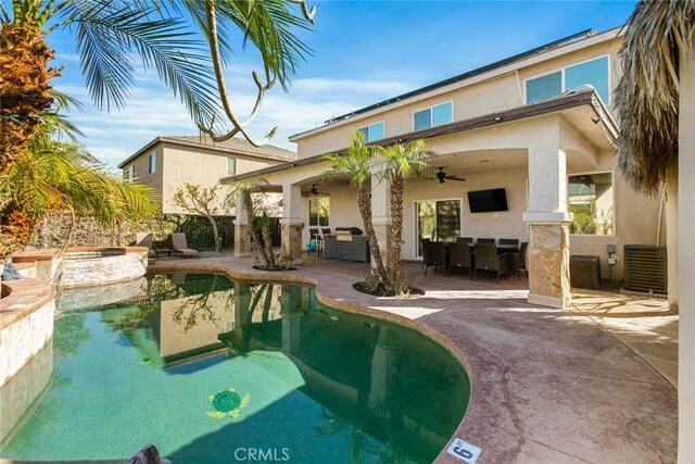 rear view of property featuring an outdoor pool, ceiling fan, a patio area, and stucco siding