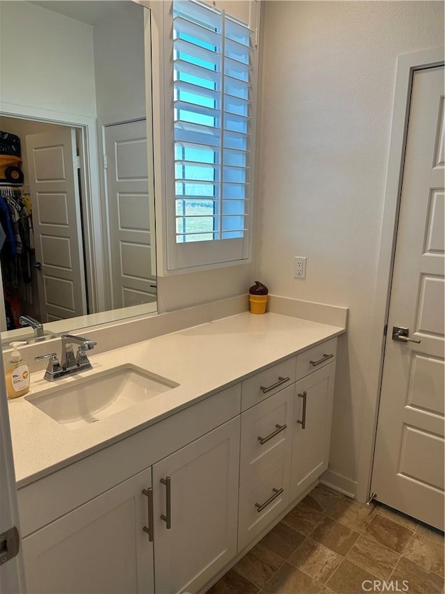 bathroom with stone finish floor, a walk in closet, and vanity