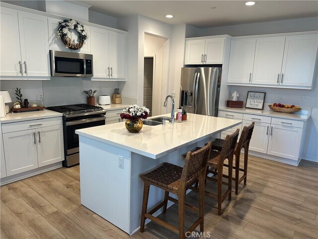 kitchen featuring stainless steel appliances, light countertops, white cabinets, a sink, and a kitchen island with sink