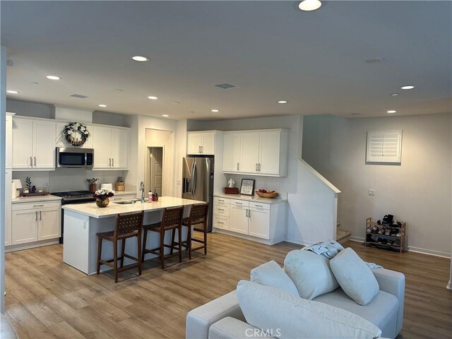 13906 Gazania Ln, Fontana, CA 92336 - kitchen with appliances with stainless steel finishes, light wood finished floors, a kitchen breakfast bar, white cabinetry, and recessed lighting