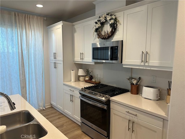 kitchen with light wood-style flooring, appliances with stainless steel finishes, light countertops, white cabinetry, and a sink