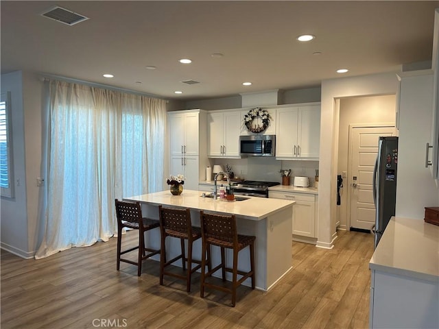 kitchen featuring a kitchen island with sink, stainless steel appliances, light countertops, and white cabinetry