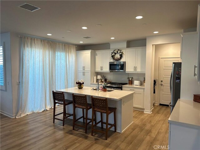 13906 Gazania Ln, Fontana, CA 92336 - kitchen with stainless steel microwave, freestanding refrigerator, light wood-style floors, white cabinets, and a breakfast bar area