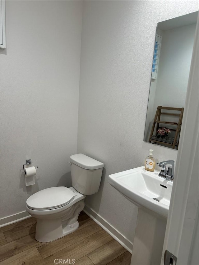 half bath featuring toilet, baseboards, and wood finished floors