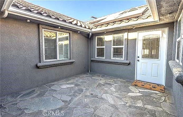 doorway to property featuring a tiled roof, a patio, and stucco siding