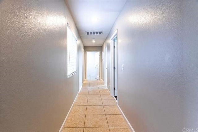 hall with a textured wall, light tile patterned flooring, visible vents, and baseboards