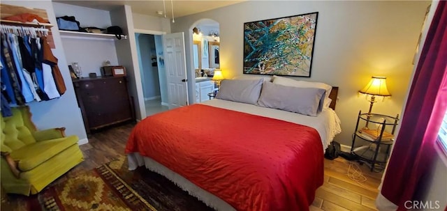 bedroom with arched walkways, a closet, baseboards, and wood finished floors