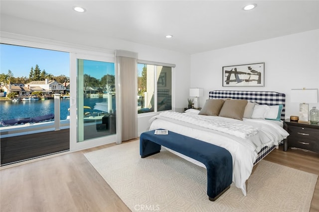 bedroom with access to exterior, recessed lighting, a water view, and light wood-style floors