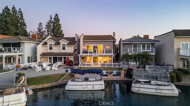 rear view of house with a patio, a water view, fence, and a tiled roof