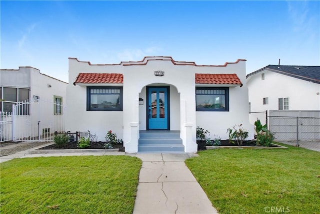 mediterranean / spanish home with a front yard, fence, and a tiled roof