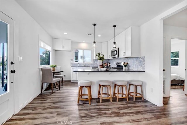 kitchen with hanging light fixtures, appliances with stainless steel finishes, dark countertops, and white cabinetry