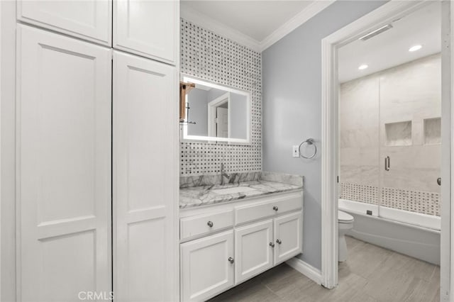 bathroom with crown molding, toilet, enclosed tub / shower combo, vanity, and baseboards