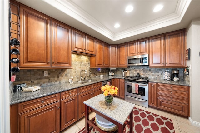 kitchen with appliances with stainless steel finishes, dark stone countertops, a raised ceiling, and brown cabinets