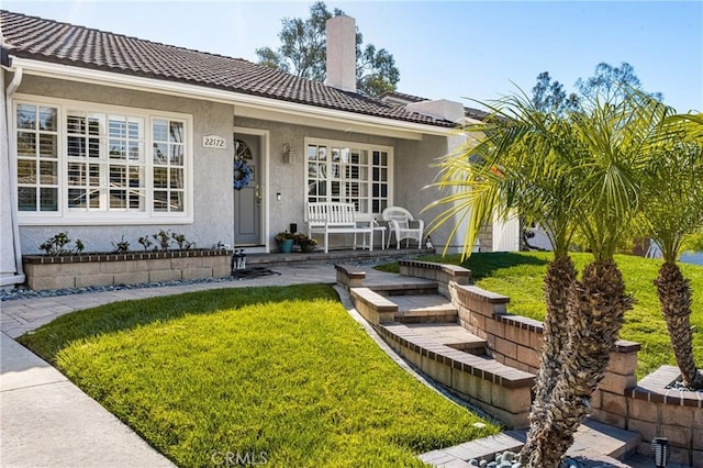 view of exterior entry featuring a chimney, a yard, a tiled roof, and stucco siding