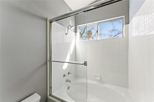 bathroom featuring a textured wall, shower / bath combination with glass door, and toilet