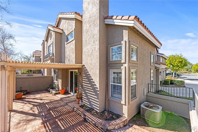 exterior space with a pergola, a tile roof, central AC unit, and stucco siding