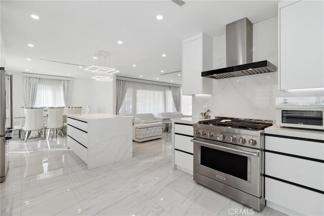 kitchen featuring pendant lighting, recessed lighting, high end stainless steel range oven, white cabinetry, and wall chimney range hood