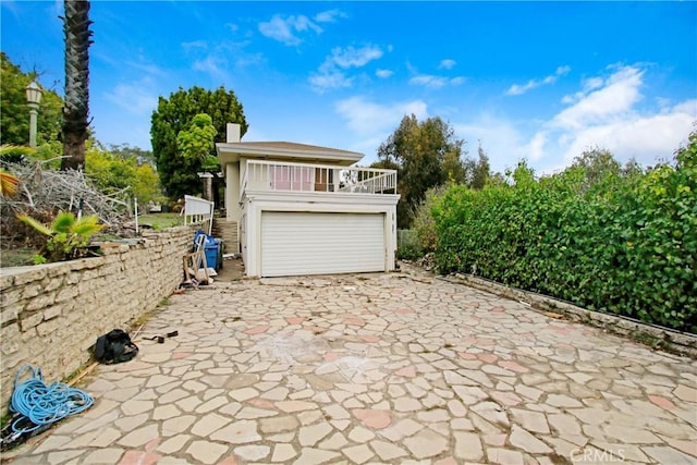 exterior space with a garage, a chimney, a balcony, and stairs