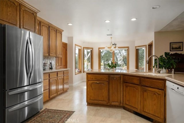 kitchen featuring freestanding refrigerator, brown cabinets, dishwasher, and a sink