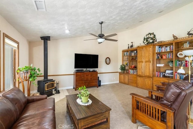 living room featuring a textured ceiling, carpet floors, visible vents, a ceiling fan, and a wood stove