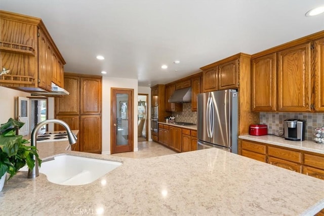 kitchen with tasteful backsplash, appliances with stainless steel finishes, brown cabinets, under cabinet range hood, and a sink