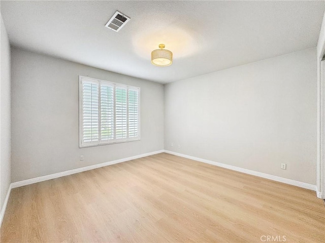 spare room featuring light wood finished floors, visible vents, and baseboards