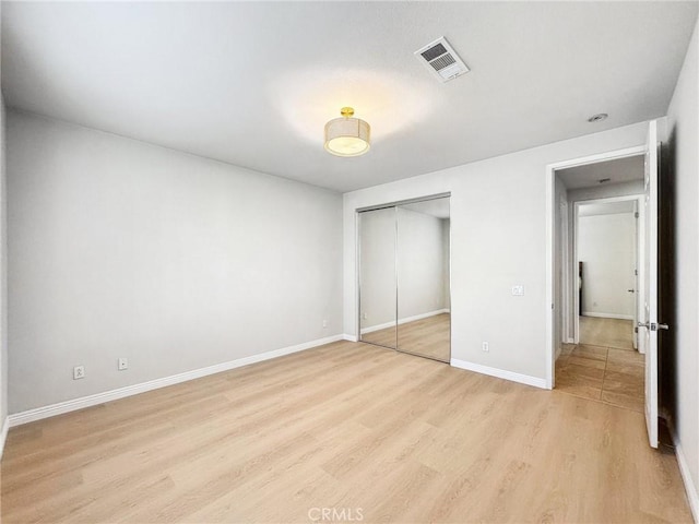 unfurnished bedroom featuring a closet, visible vents, light wood-style flooring, and baseboards