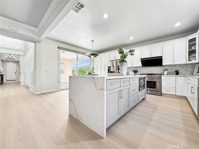 kitchen with white cabinetry, hanging light fixtures, backsplash, high end range, and glass insert cabinets