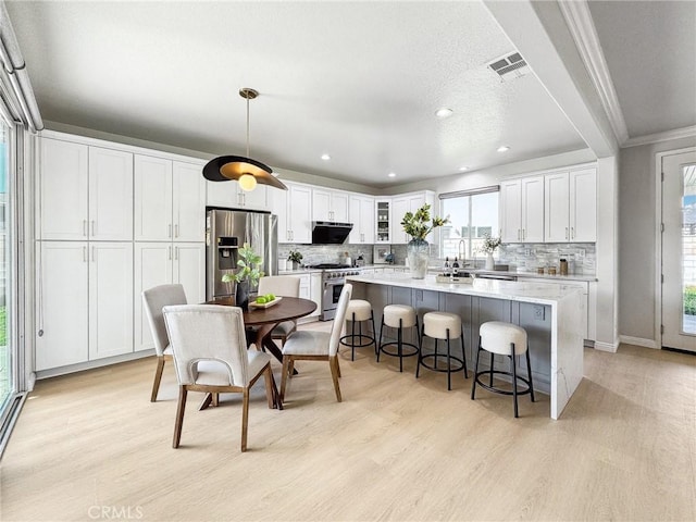 kitchen featuring glass insert cabinets, appliances with stainless steel finishes, hanging light fixtures, light countertops, and white cabinetry