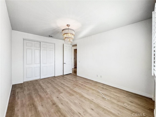 unfurnished bedroom with a notable chandelier, visible vents, baseboards, light wood-style floors, and a closet