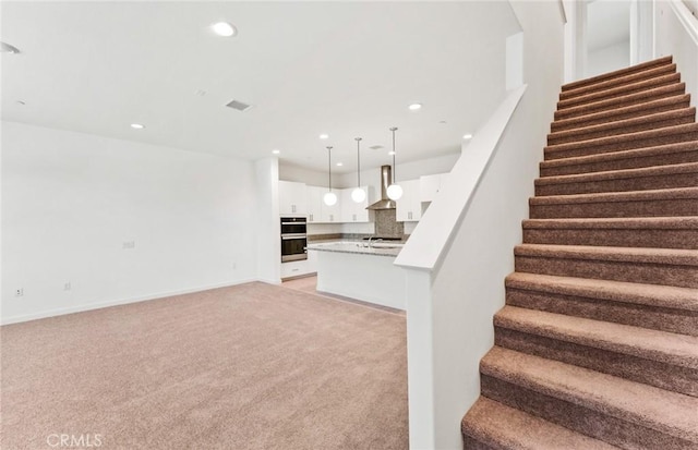 interior space featuring recessed lighting, light colored carpet, a sink, baseboards, and stairway