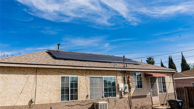 back of house with roof mounted solar panels, roof with shingles, and stucco siding