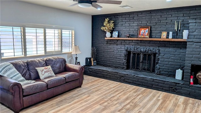 living room with a ceiling fan, light wood-type flooring, visible vents, and a brick fireplace