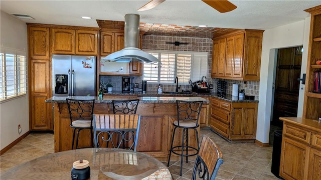 kitchen featuring visible vents, decorative backsplash, a kitchen island, island range hood, and stainless steel fridge