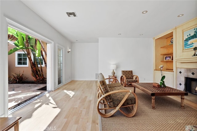 sitting room with built in shelves, a fireplace, light wood finished floors, recessed lighting, and visible vents