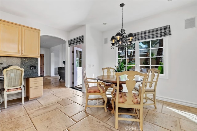 dining area featuring arched walkways, a chandelier, visible vents, baseboards, and stone tile flooring