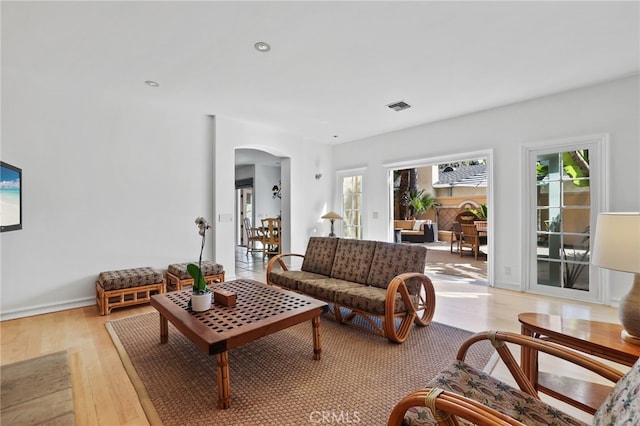 living area featuring light wood finished floors, visible vents, arched walkways, and recessed lighting