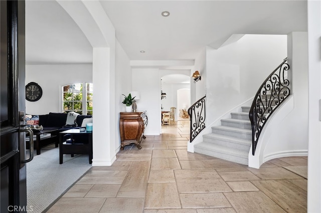 entryway with arched walkways, stone tile flooring, baseboards, and stairs