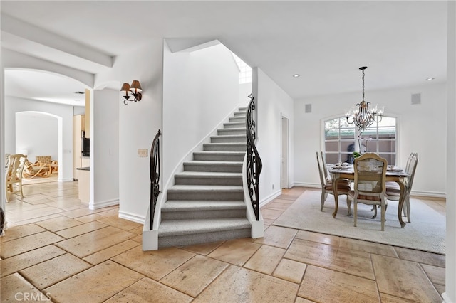 dining room featuring a chandelier, stone tile flooring, baseboards, and stairs