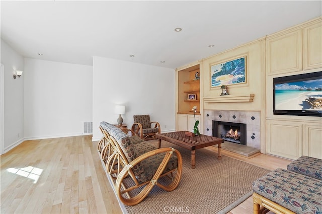 sitting room featuring built in shelves, a tile fireplace, visible vents, baseboards, and light wood-type flooring