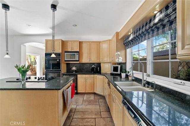 kitchen with dark countertops, stainless steel microwave, hanging light fixtures, a sink, and dishwasher