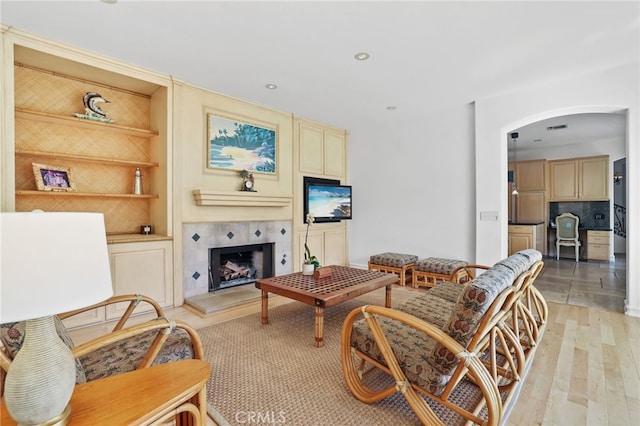 living area featuring built in features, arched walkways, recessed lighting, light wood-type flooring, and a tile fireplace