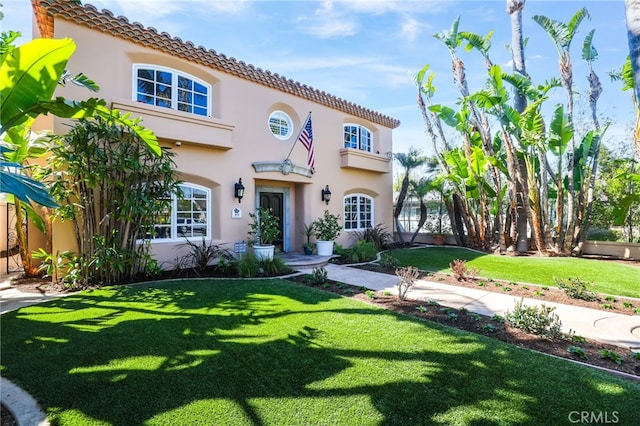 mediterranean / spanish-style house featuring a tiled roof, a front yard, and stucco siding