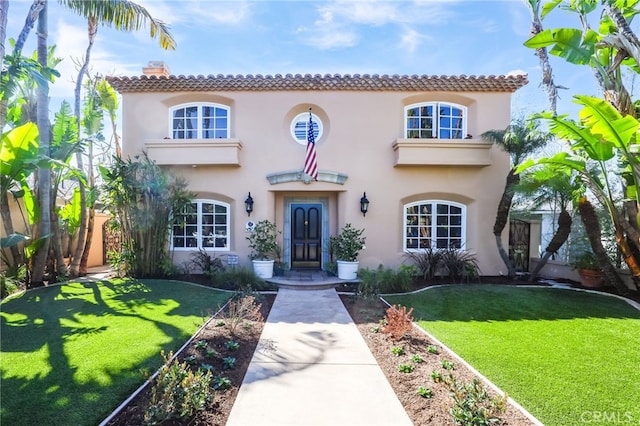 mediterranean / spanish house with a tile roof, a chimney, a front lawn, and stucco siding