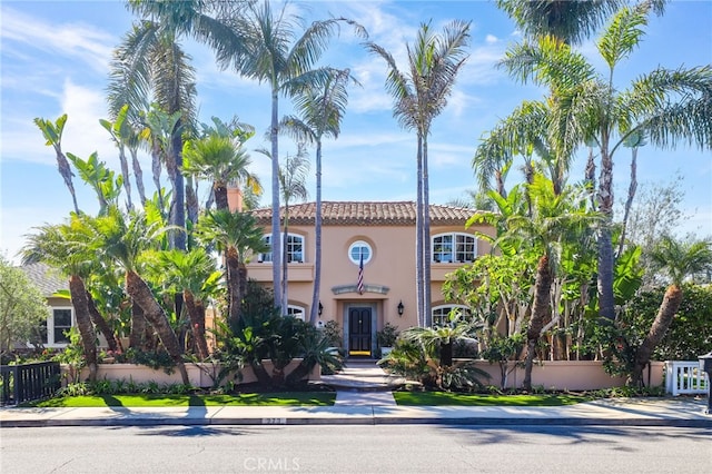 mediterranean / spanish house with a tile roof, fence, and stucco siding