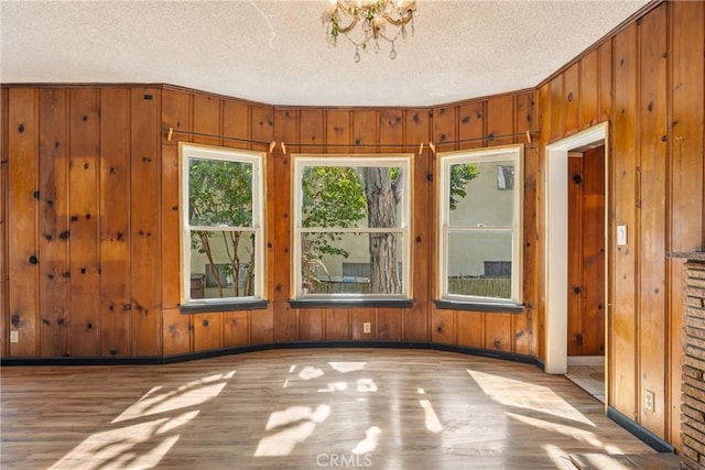 empty room featuring a textured ceiling, wooden walls, wood finished floors, and baseboards