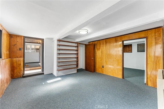 unfurnished room featuring carpet floors, wooden walls, stairway, and beam ceiling