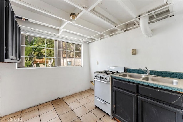 kitchen featuring a sink, light tile patterned floors, dark cabinetry, and gas range gas stove