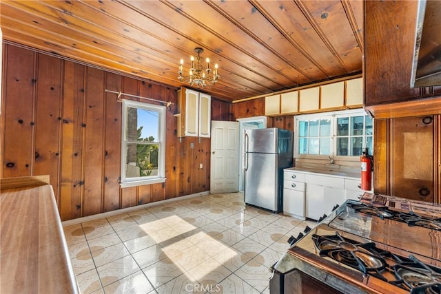 kitchen with light tile patterned floors, a notable chandelier, wood ceiling, white cabinetry, and freestanding refrigerator