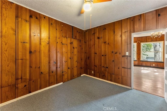 unfurnished room featuring carpet floors, wood walls, a textured ceiling, and ceiling fan with notable chandelier